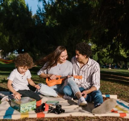 A joyful family enjoying a summer picnic with a ukulele in a sunny park setting.