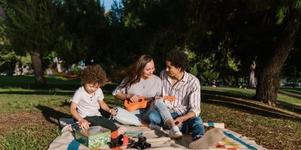 A joyful family enjoying a summer picnic with a ukulele in a sunny park setting.