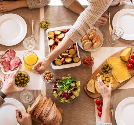 Overhead view of a diverse cheese platter setup for a delicious meal, featuring fresh produce and juices on a table.