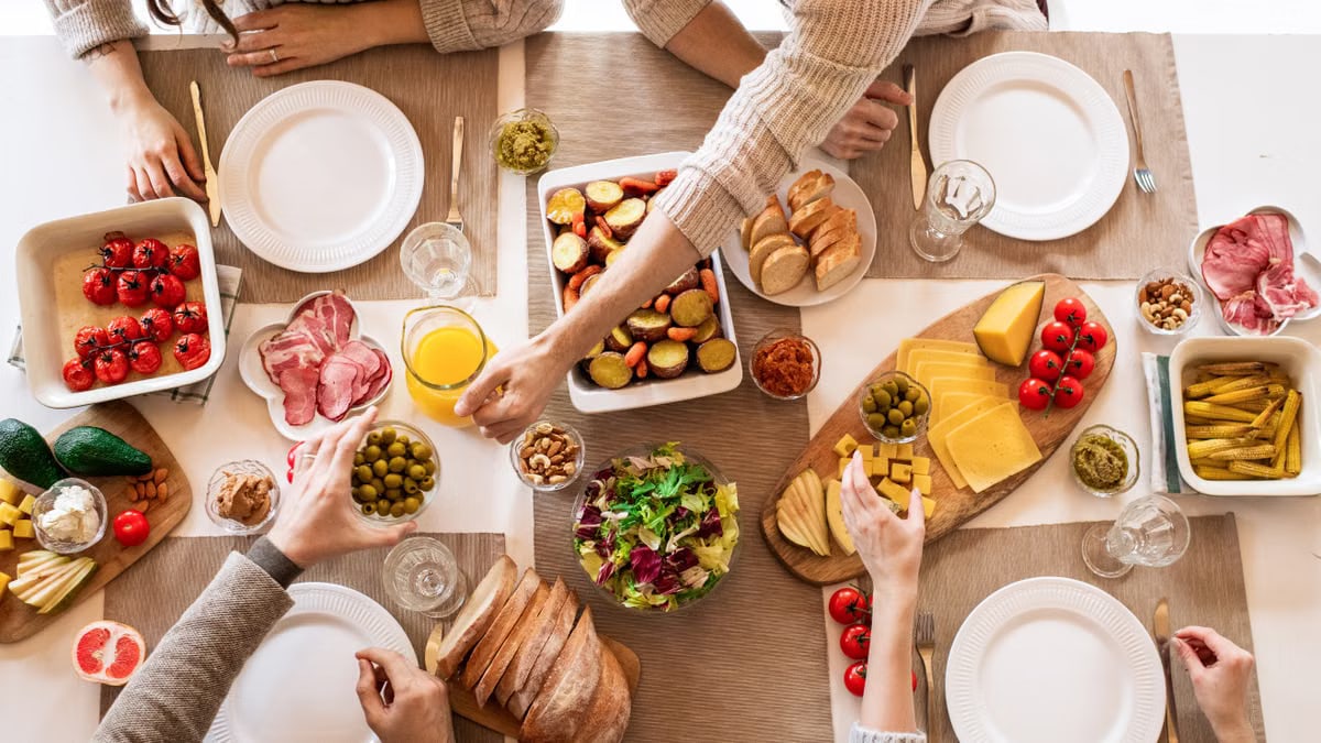 Overhead view of a diverse cheese platter setup for a delicious meal, featuring fresh produce and juices on a table.
